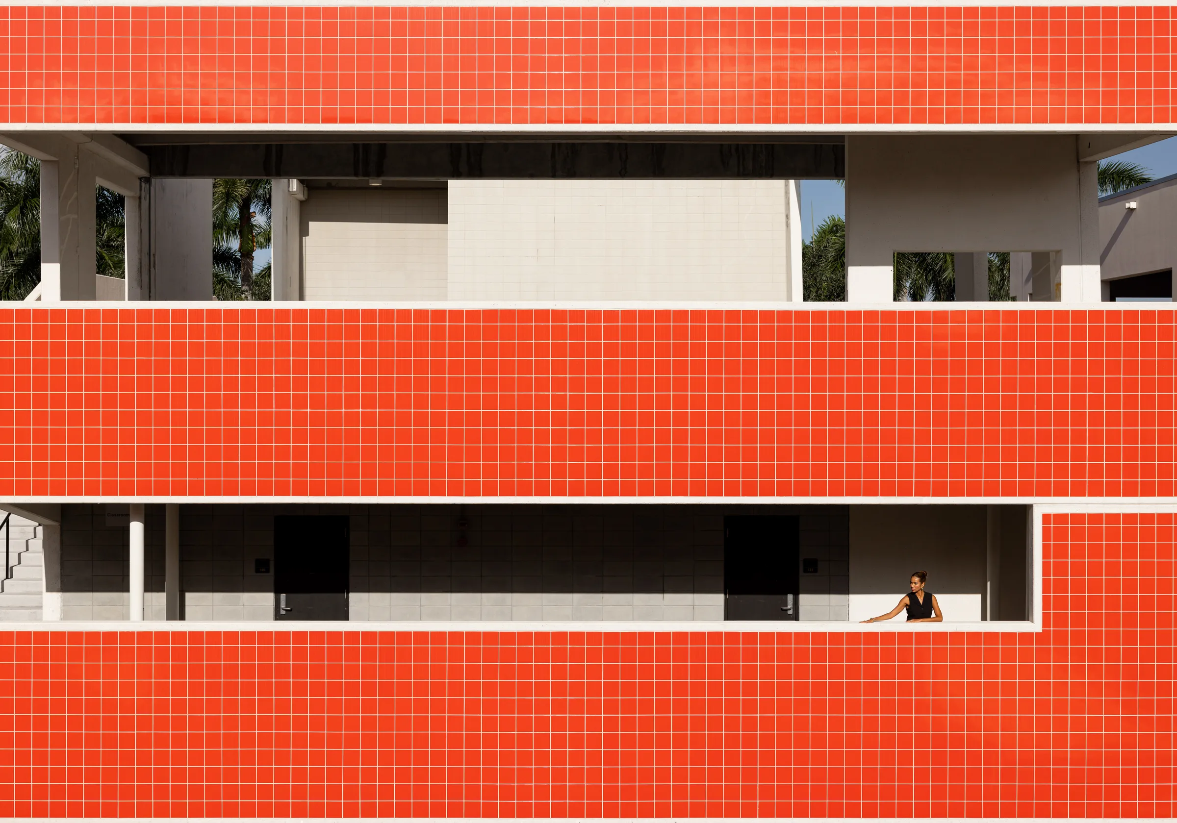 Woman in a black dress standing in a window opening of a building faced in bright orange tile, by ARCHTRAITS