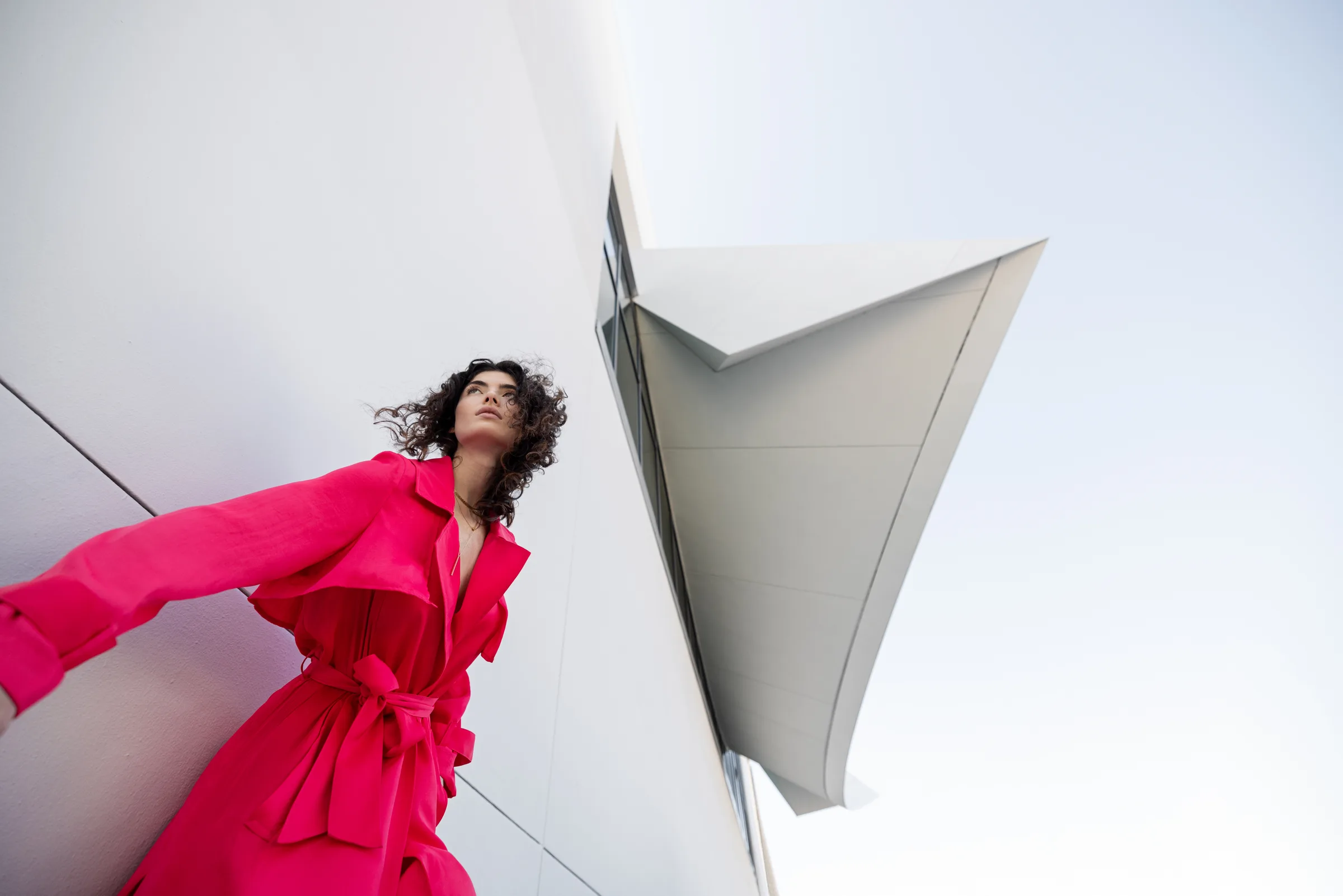Woman in a flowing pink dress against a sharp, angular white building facade, by ARCHTRAITS