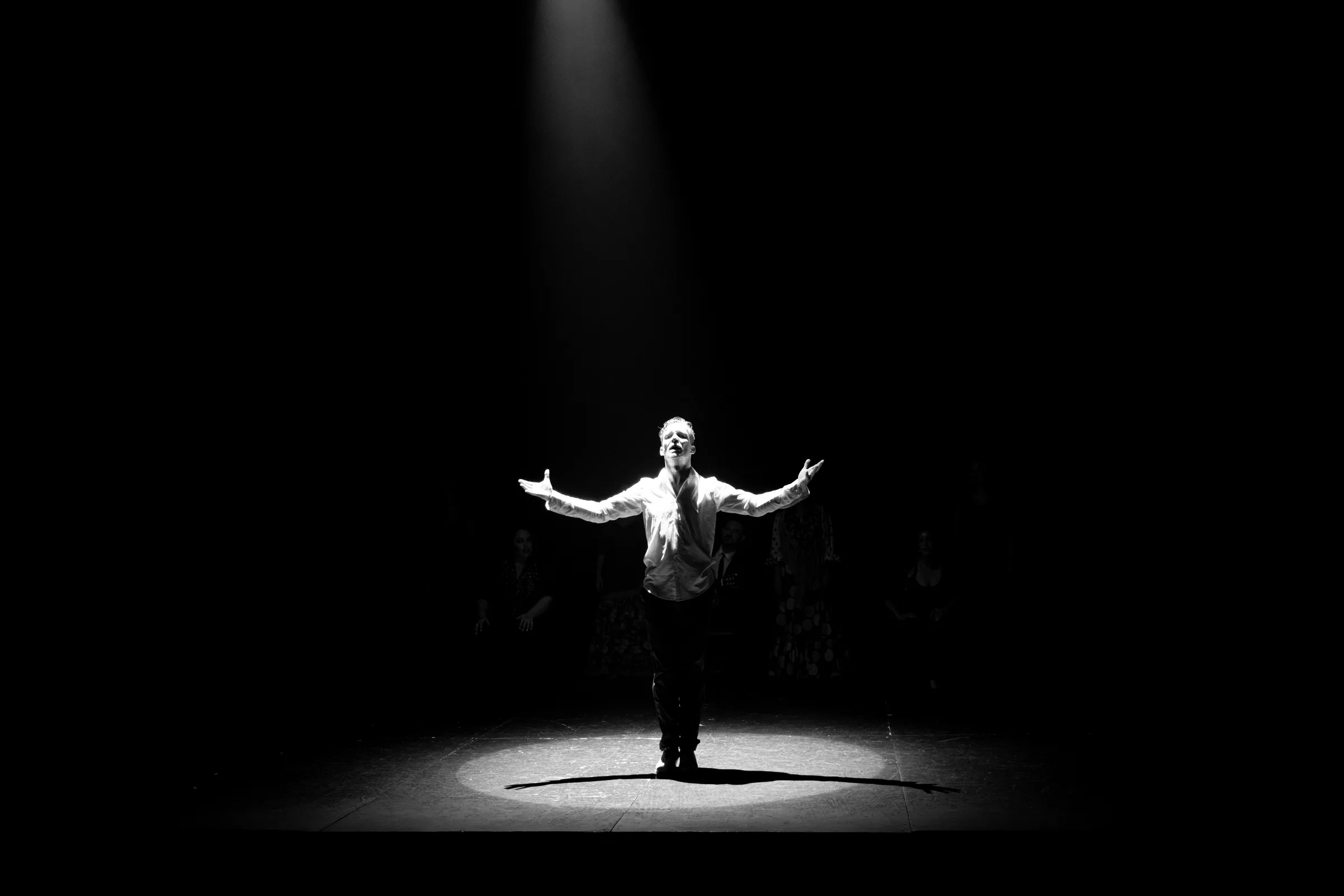 Silhouette of a dancer with arms outstretched under a single spotlight, by ARCHTRAITS