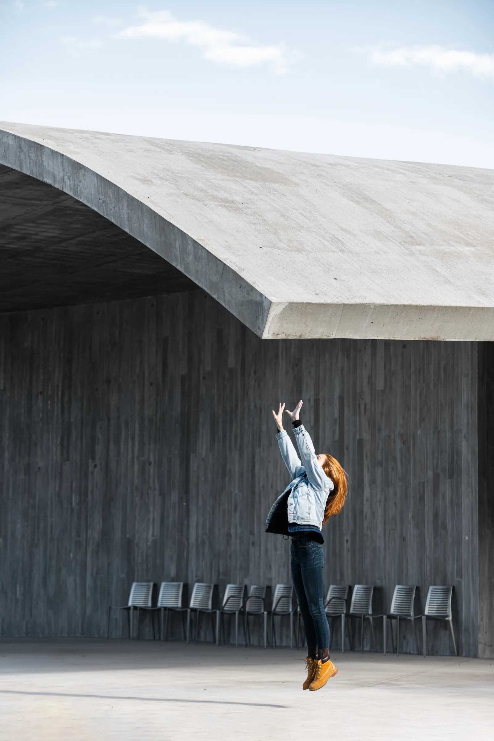 Woman jumping and reaching toward a sweeping curved concrete roof, Winter Park Library, Florida, by ARCHTRAITS