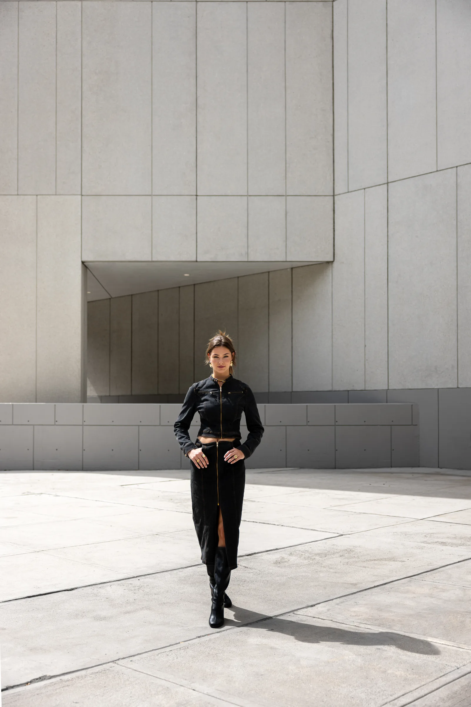Woman in a black jacket and skirt standing in a minimalist concrete plaza, architecture photography by ARCHTRAITS