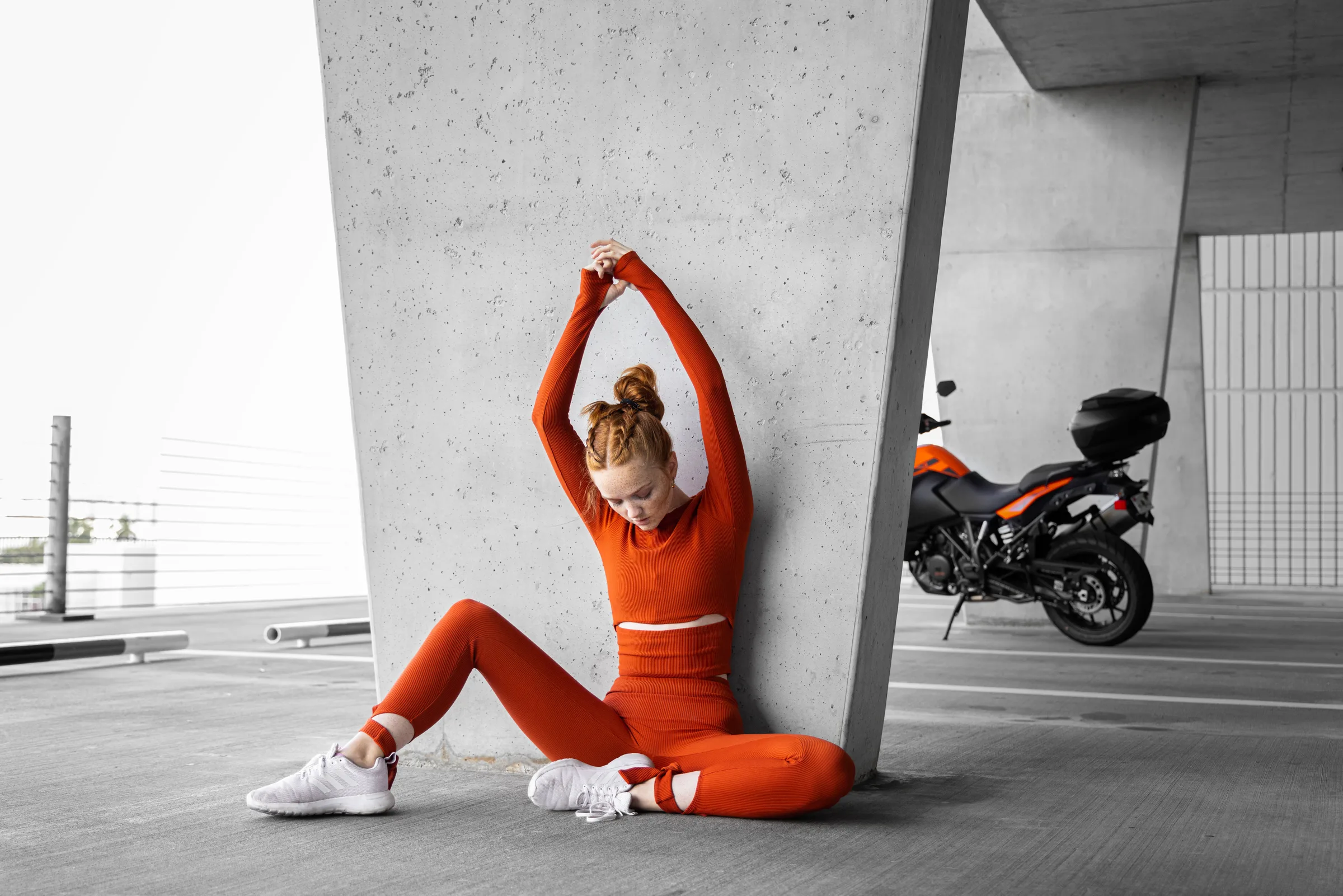 Woman in red stretching against a concrete column, a motorcycle parked in the background at 1111 Lincoln Road, Miami Beach, by ARCHTRAITS