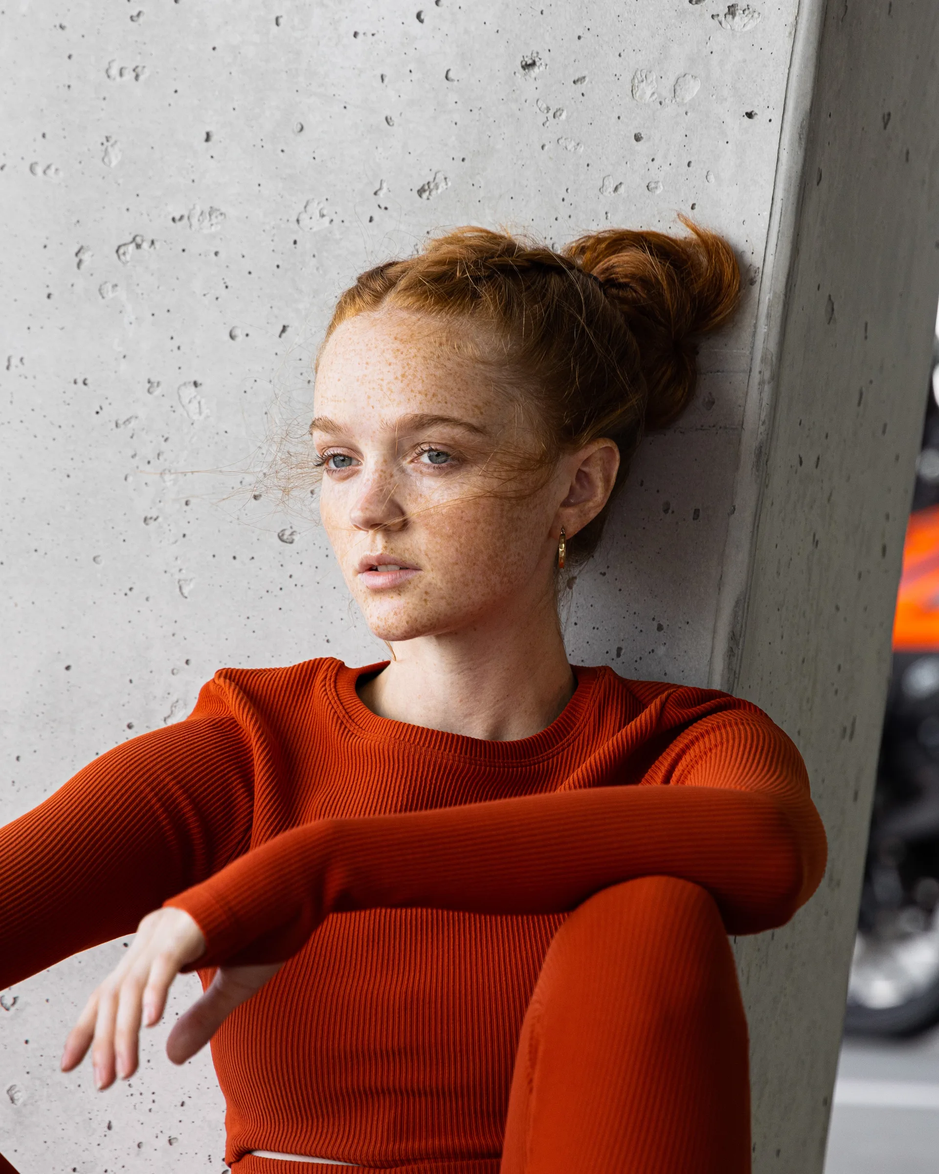 Close portrait of a woman in red leaning against a concrete column, a motorcycle parked behind her, at 1111 Lincoln Road, Miami Beach, by ARCHTRAITS