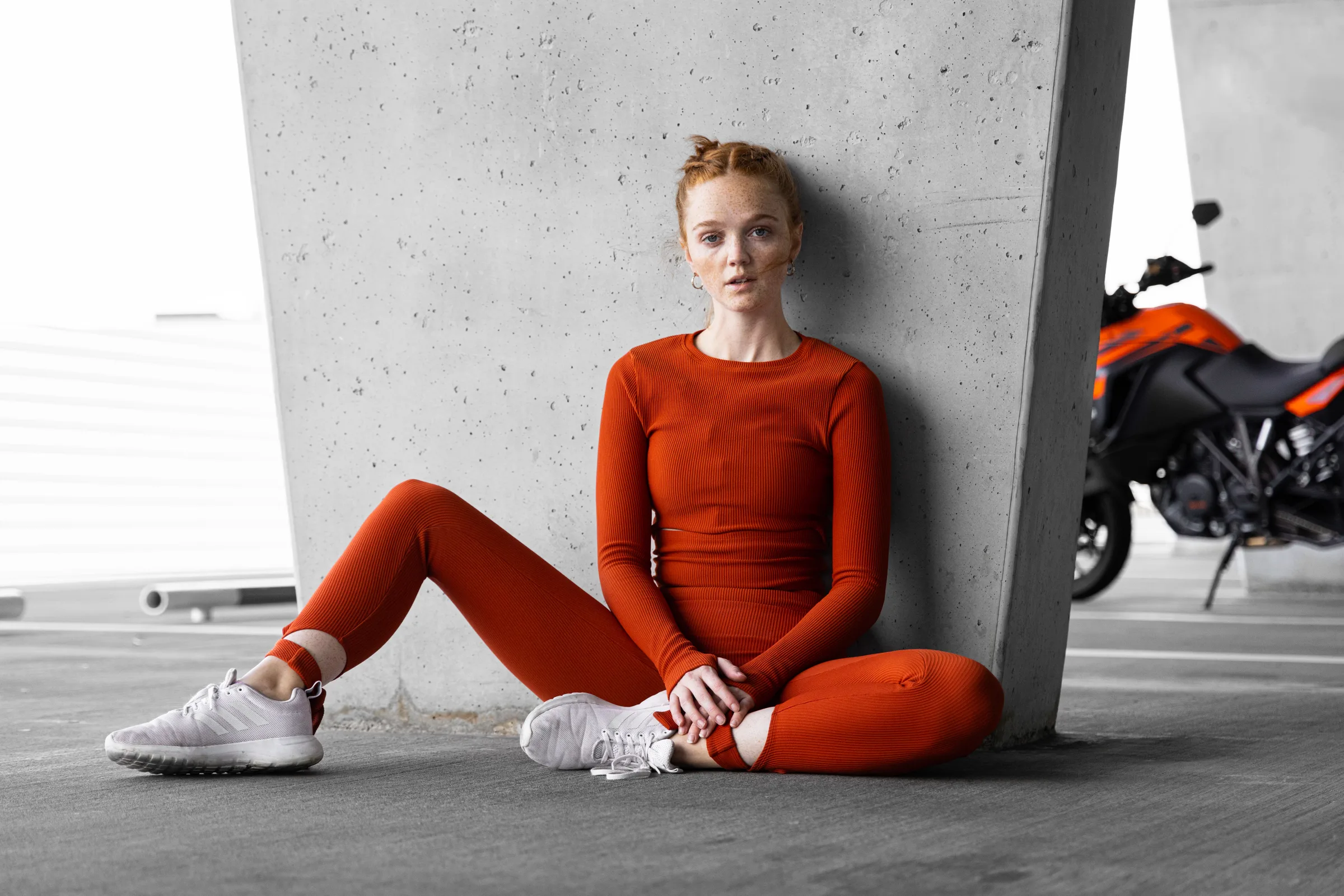 Woman in red sitting cross-legged against a concrete column with a motorcycle parked behind her, 1111 Lincoln Road, Miami Beach, by ARCHTRAITS