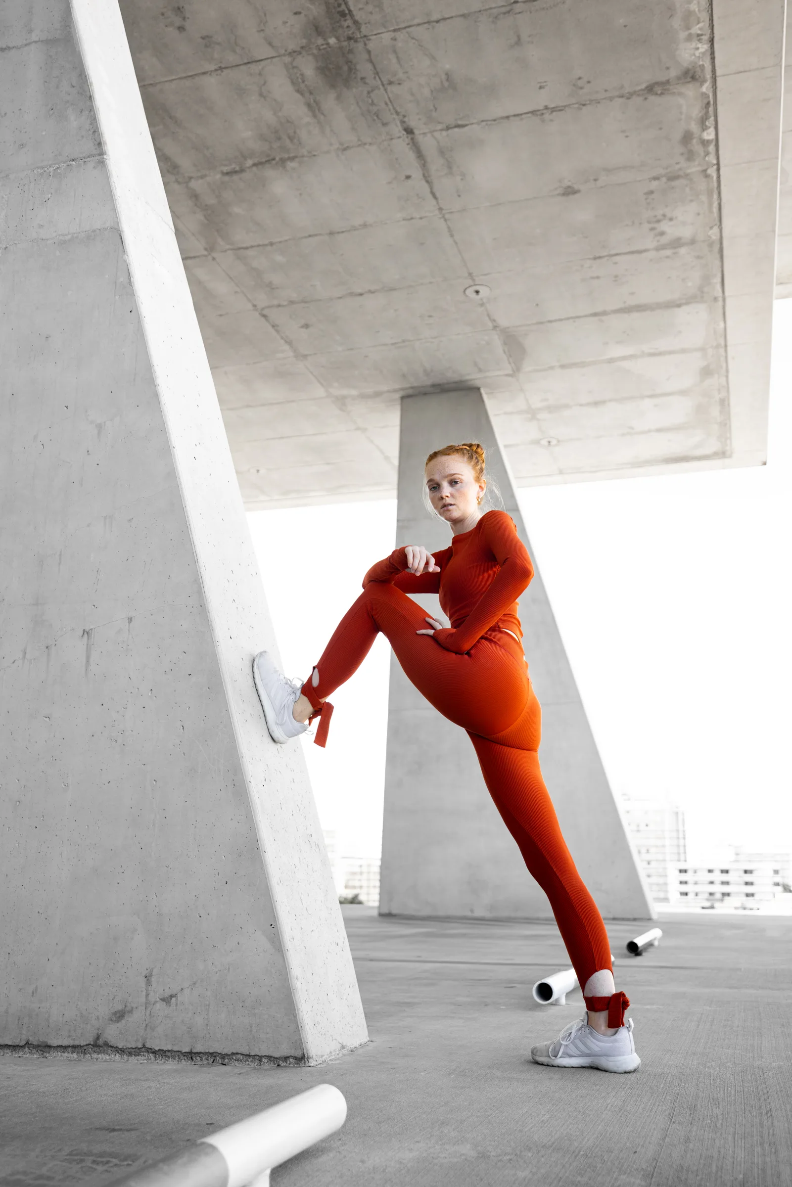 Woman in red kicking one leg up against a diagonal concrete column, triangular pillars of 1111 Lincoln Road in the background, Miami Beach, by ARCHTRAITS