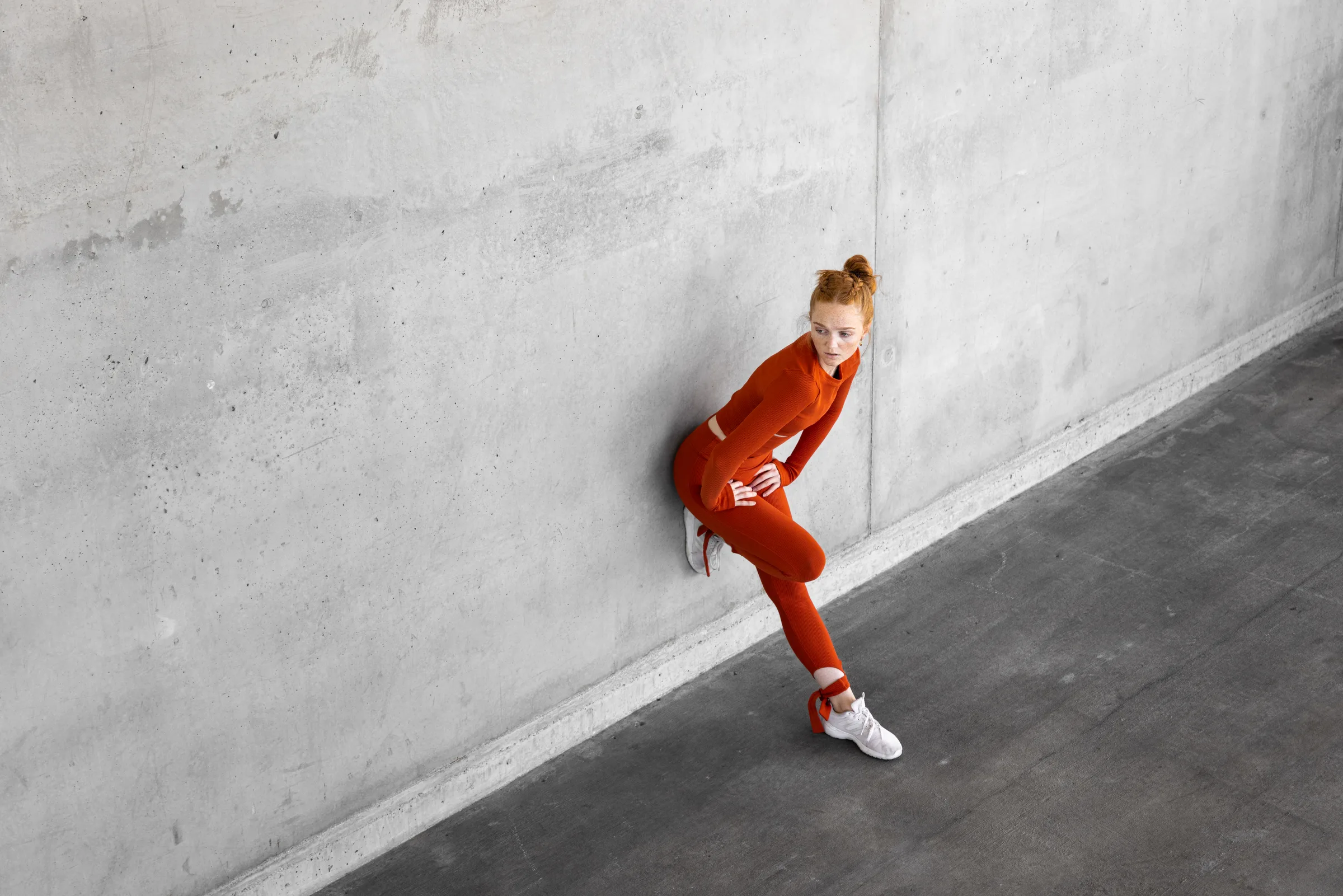 Aerial view of a woman in red leaning against a concrete wall with one leg raised, in a receding hallway at 1111 Lincoln Road, Miami Beach, by ARCHTRAITS