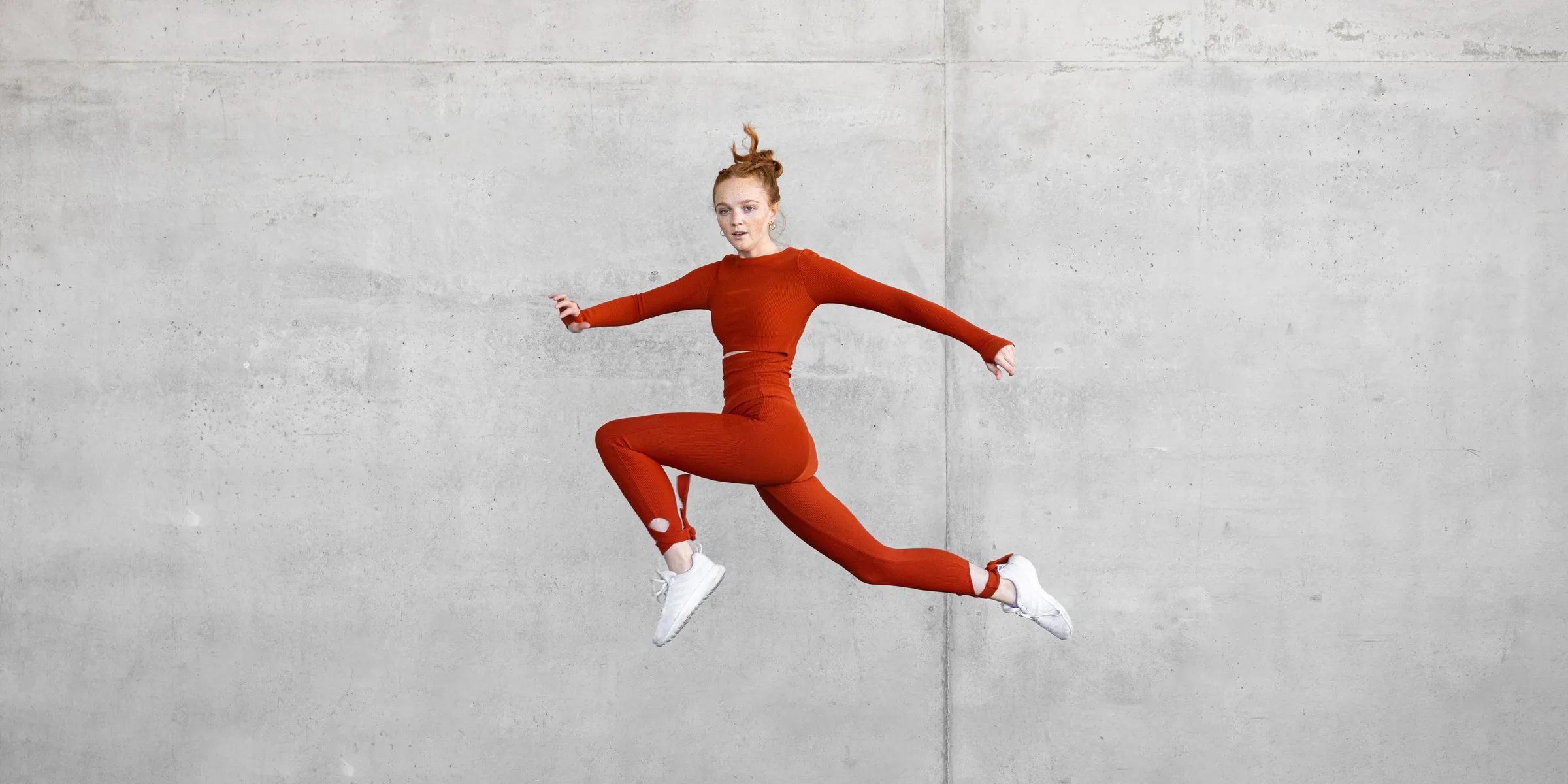 Woman in red performing a high kick against a concrete wall, composed to look like she's climbing it, at 1111 Lincoln Road, Miami Beach, by ARCHTRAITS