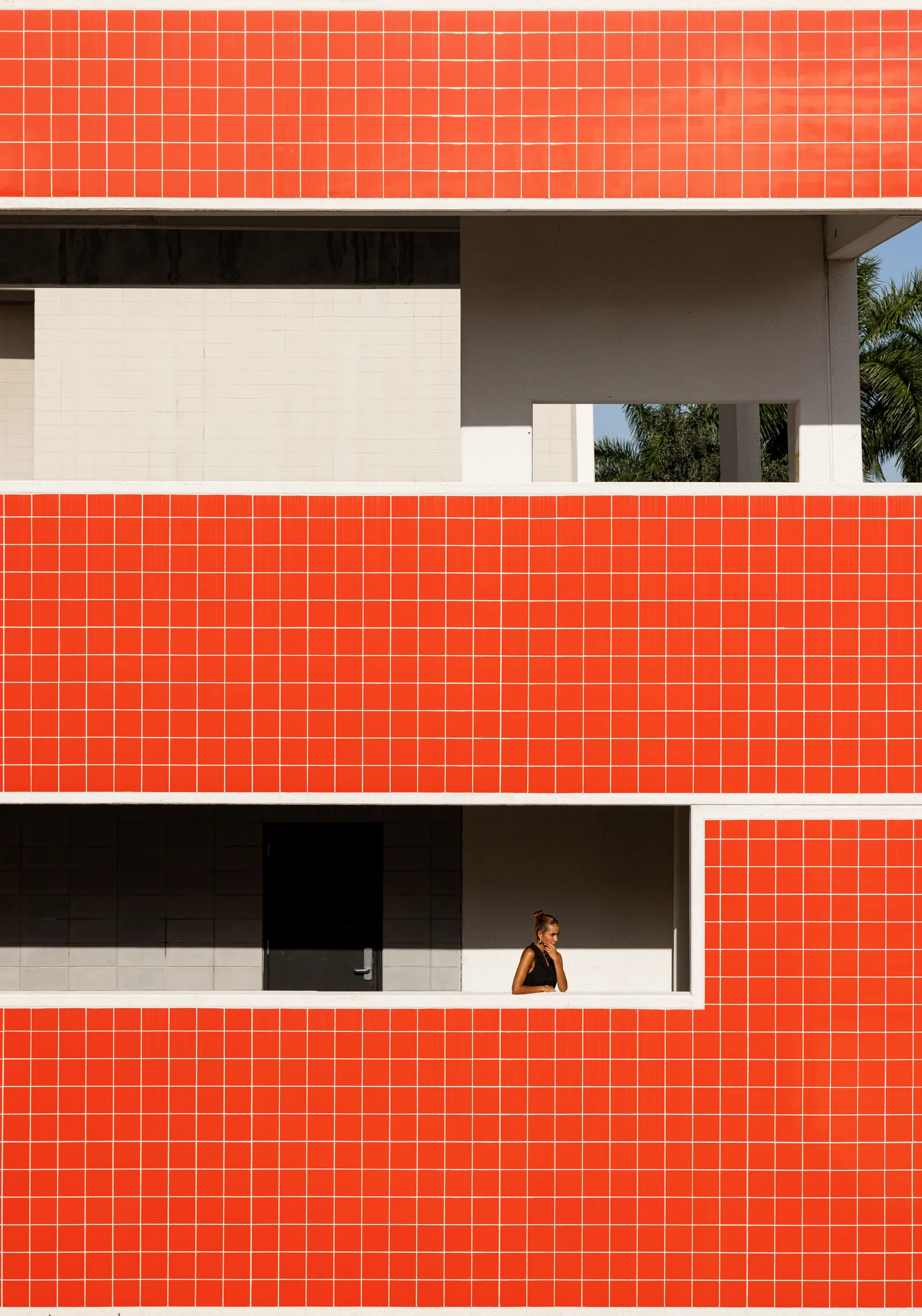 Woman standing in a window opening of an orange tile facade at FIU School of Architecture, Miami, by ARCHTRAITS