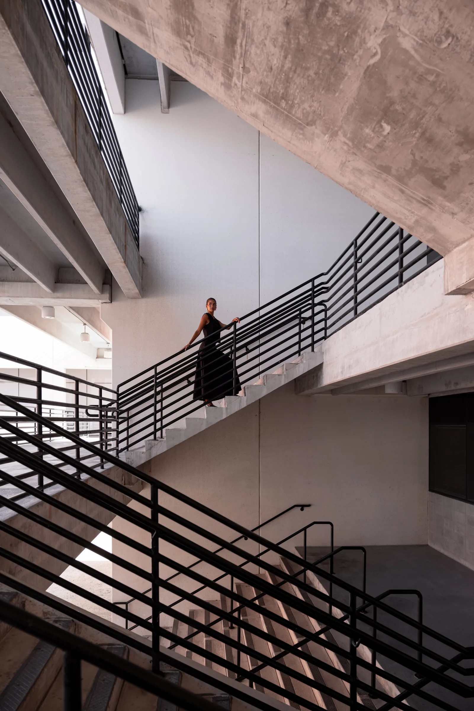 Woman descending a concrete staircase with black railings at FIU School of Architecture, Miami, by ARCHTRAITS