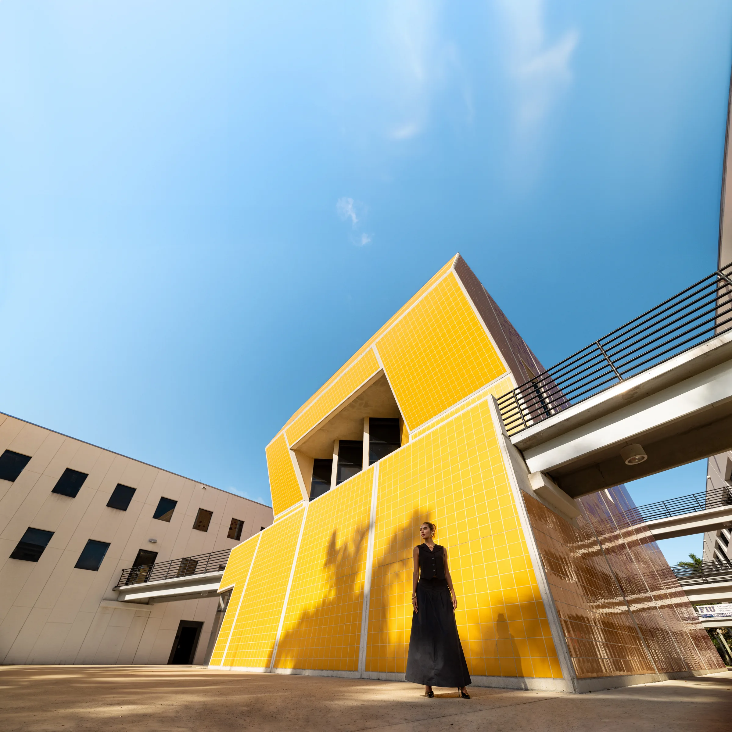 Woman standing at the base of a dramatic yellow-tiled triangular volume at FIU School of Architecture, Miami, by ARCHTRAITS