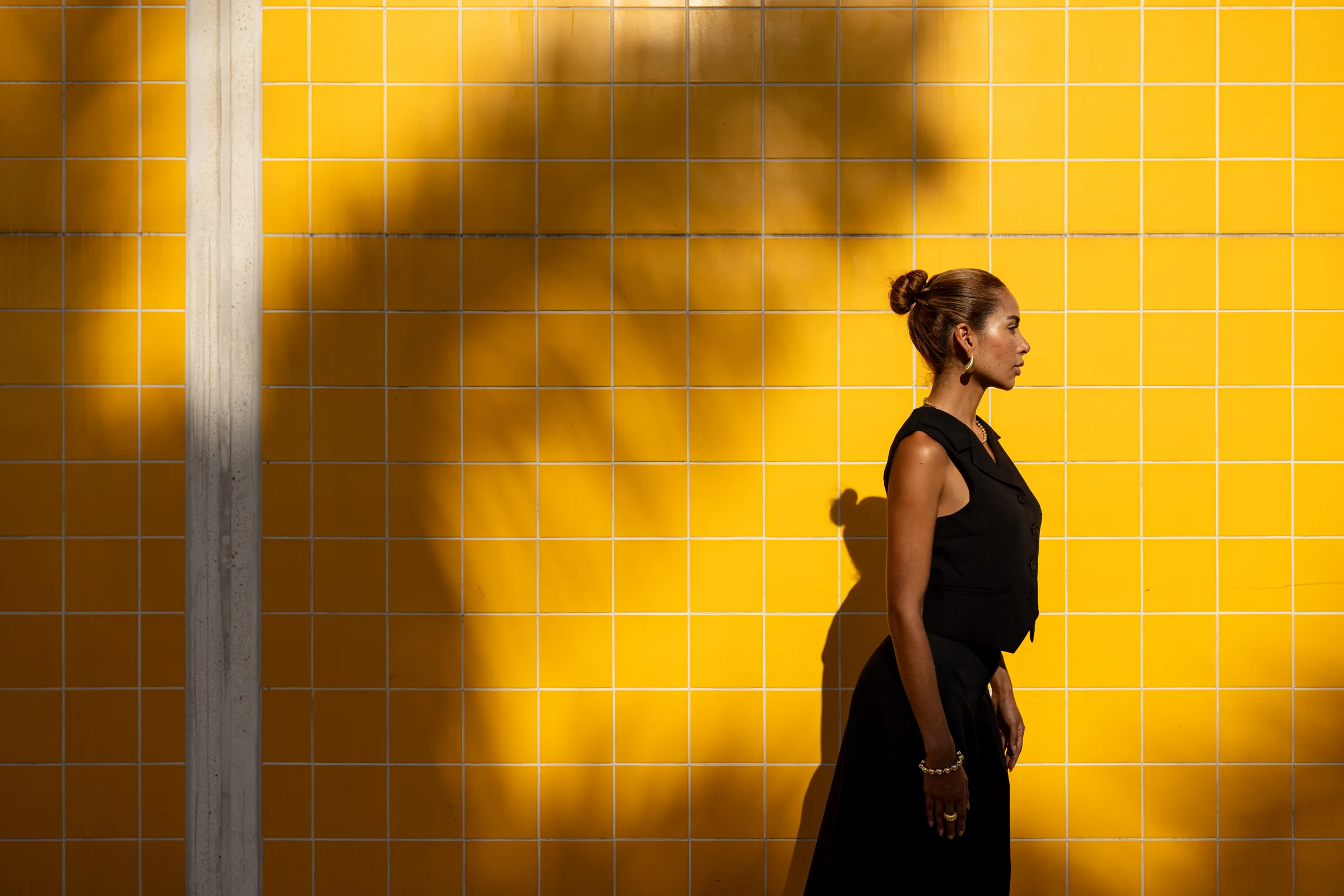 Woman in profile against a sunlit yellow tile wall with a tree shadow, FIU School of Architecture, Miami, by ARCHTRAITS