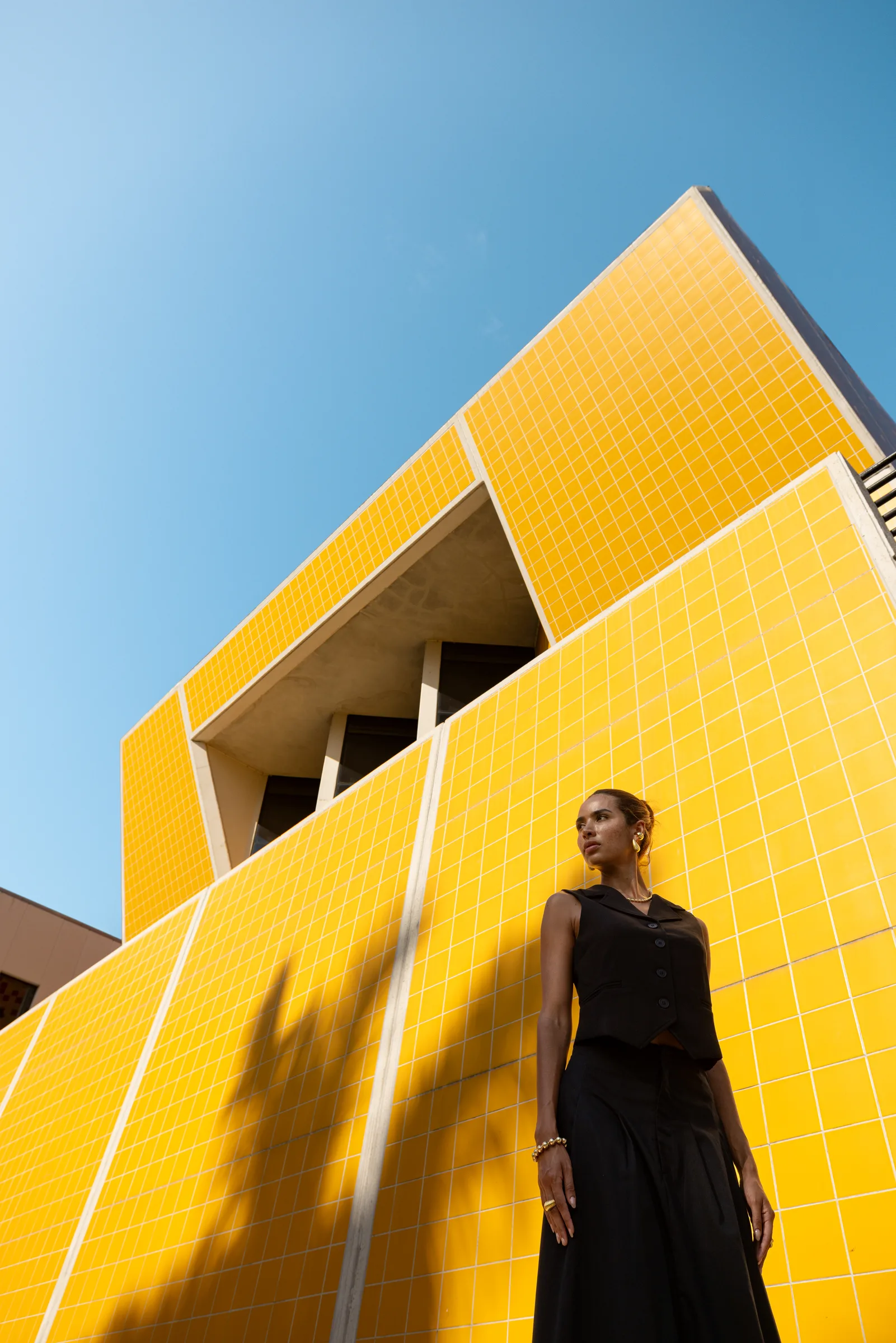 Woman standing against a yellow-tiled triangular volume looking upward, FIU School of Architecture, Miami, by ARCHTRAITS