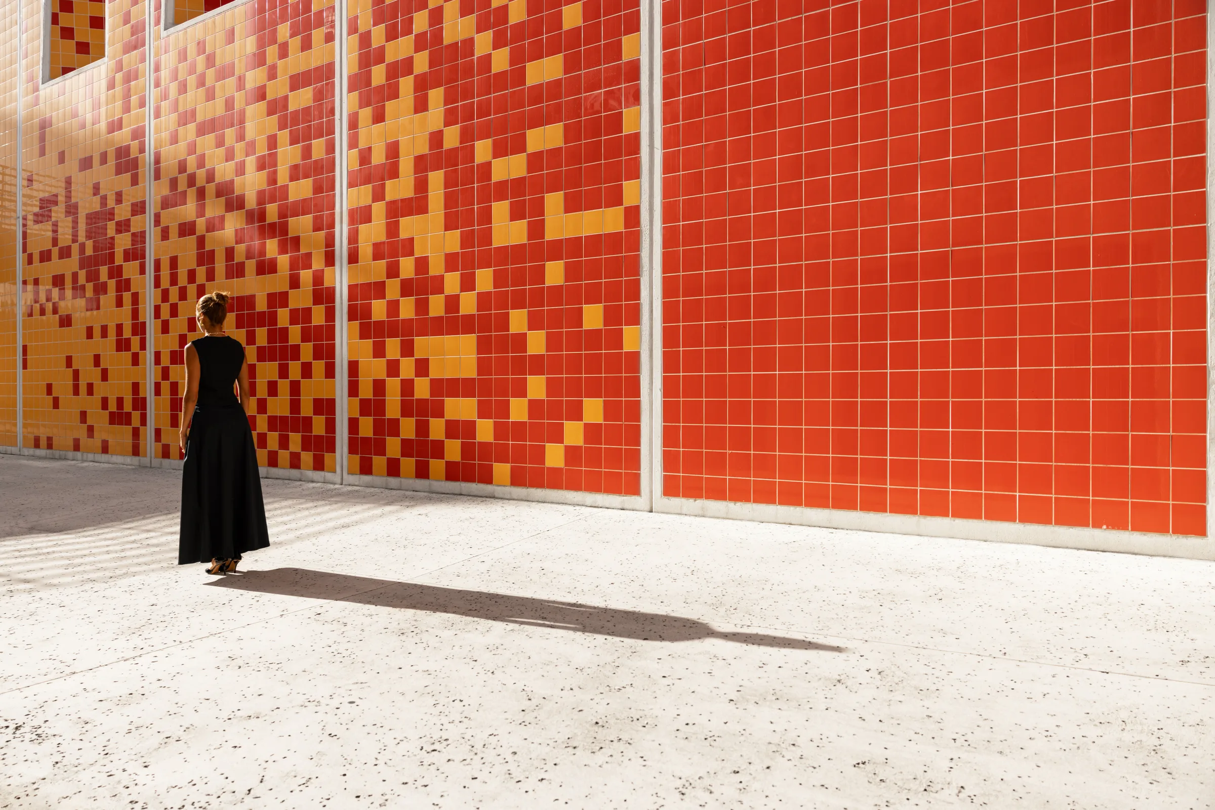 Woman walking away from a red-and-yellow checkerboard tile wall at FIU School of Architecture, Miami, by ARCHTRAITS