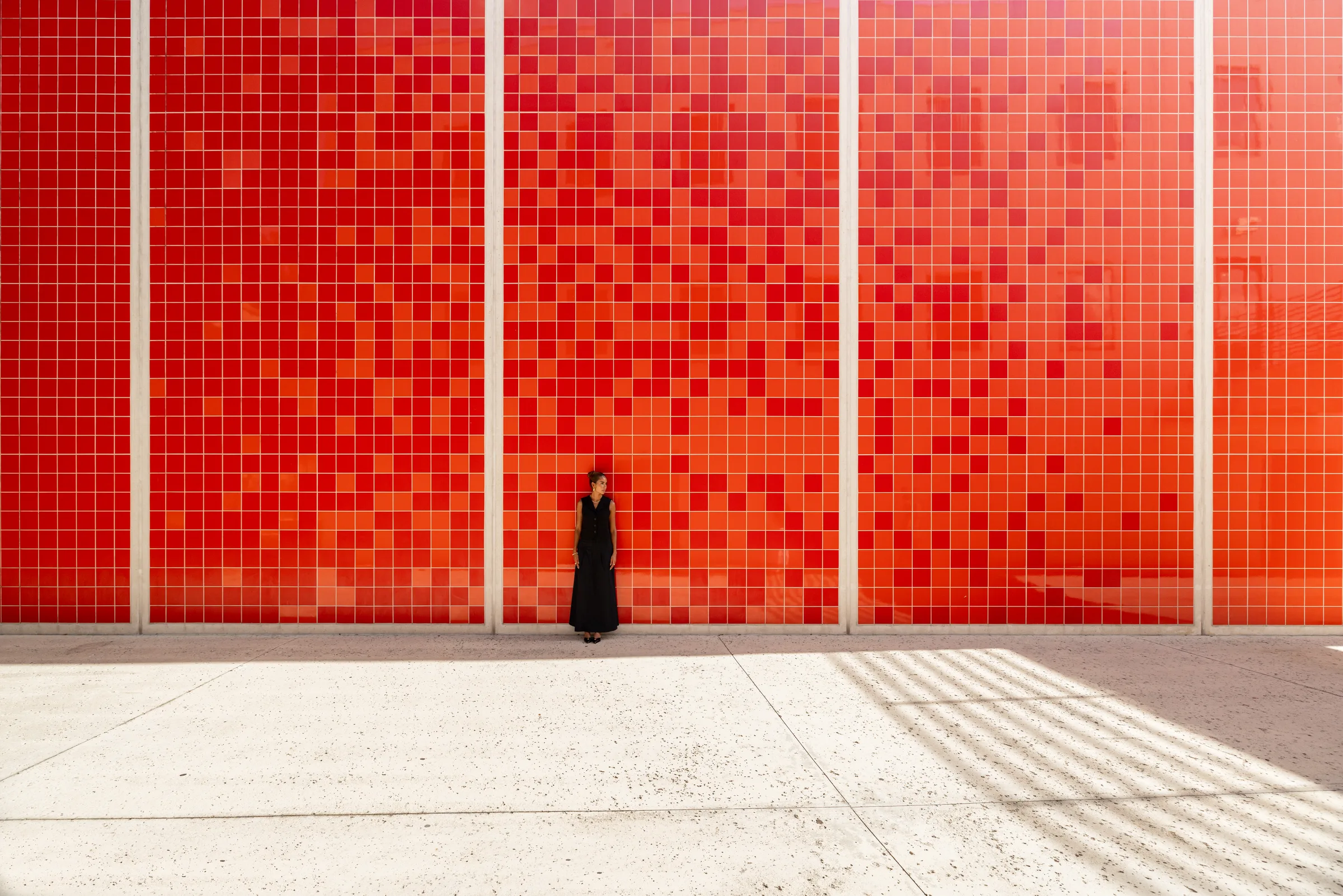 Woman standing small against a towering red tile wall at FIU School of Architecture, Miami, by ARCHTRAITS