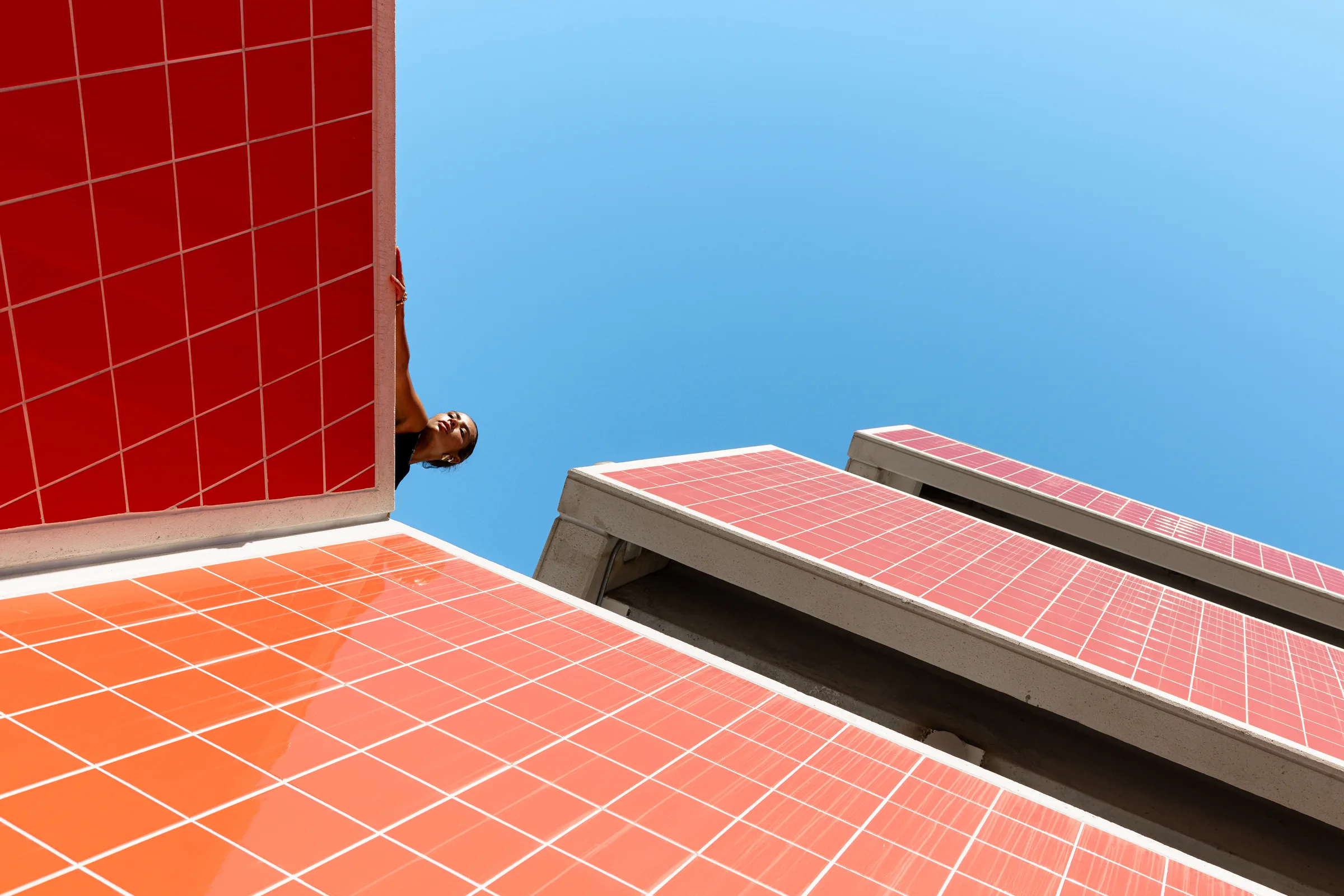 Looking up at a red tile wall corner and pink canopy edges with a woman peeking around it, FIU School of Architecture, Miami, by ARCHTRAITS
