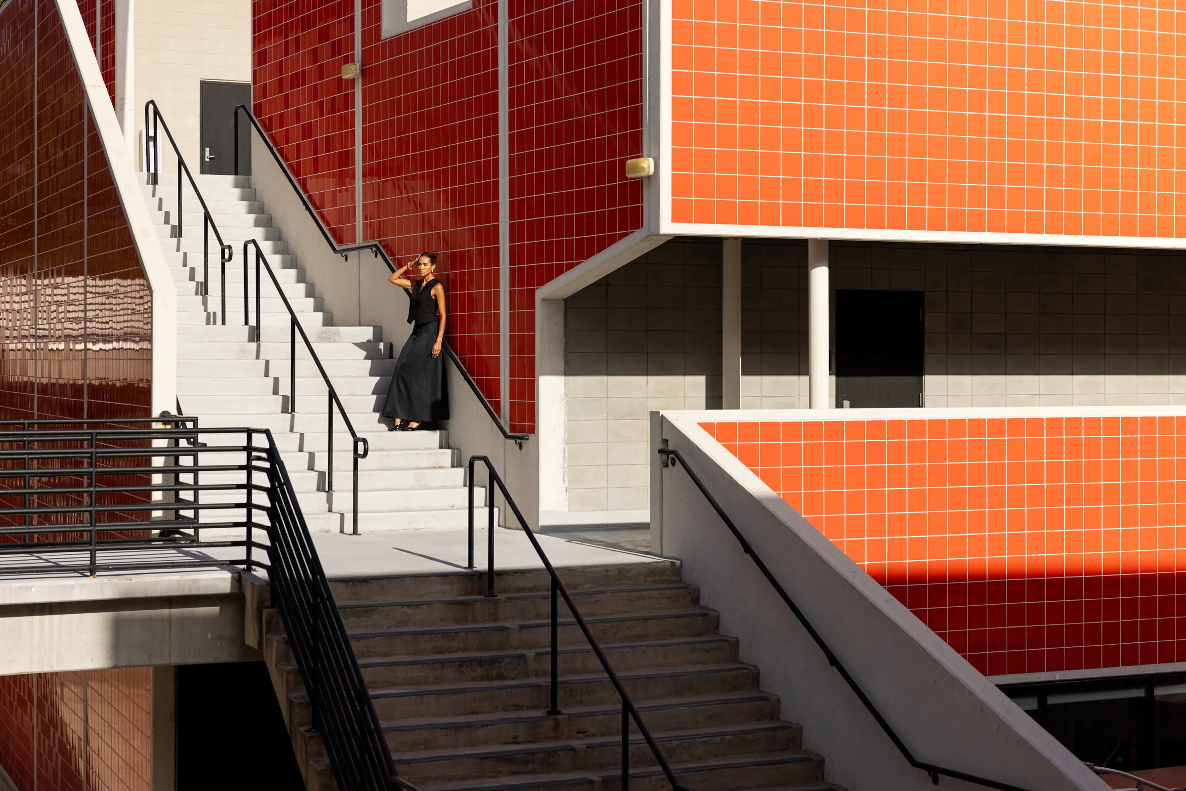 Woman standing on a concrete staircase against a red tile wall at FIU School of Architecture, Miami, by ARCHTRAITS