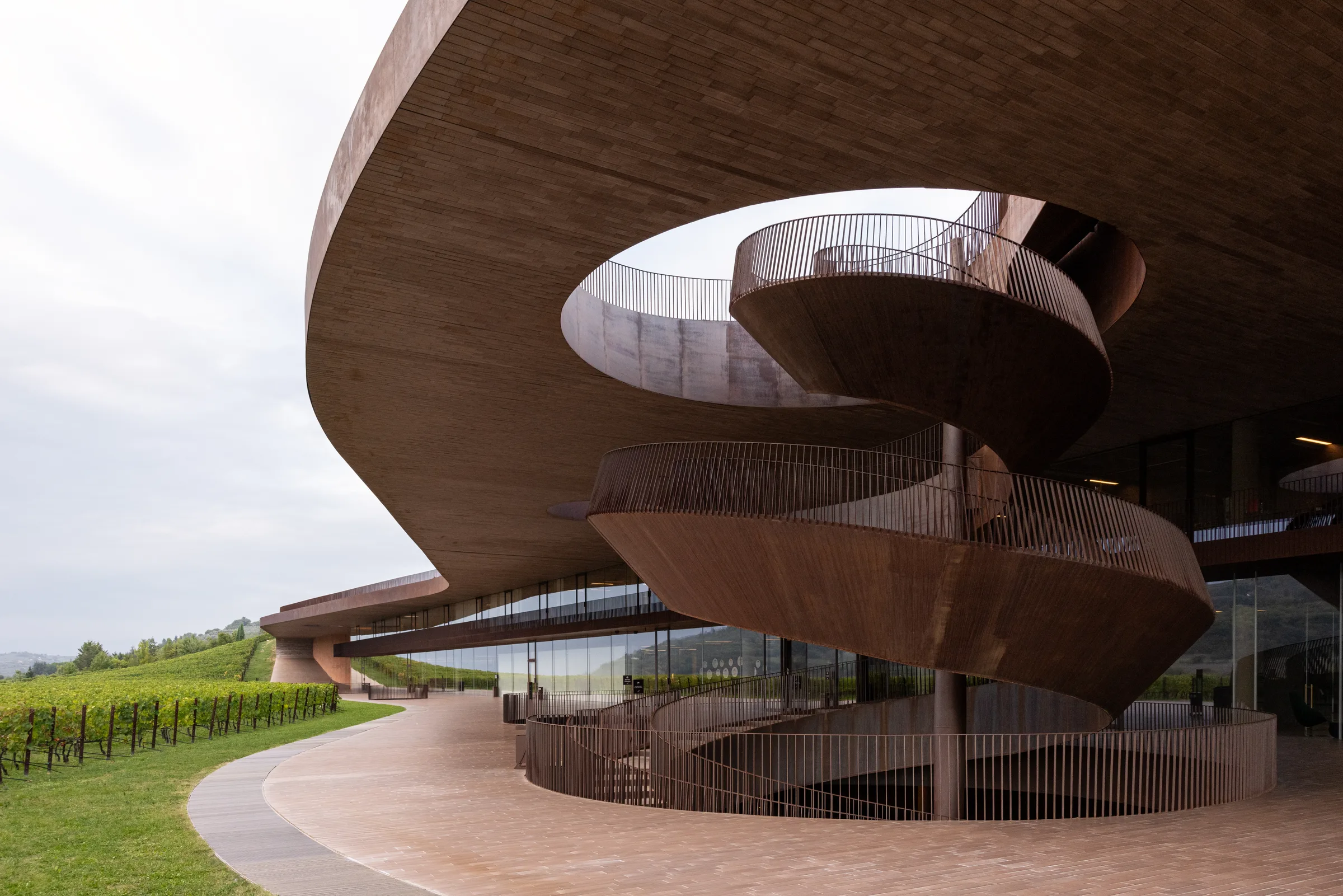 Wide view of Cantina Antinori's spiraling corten steel staircase beneath its sweeping cantilevered roof, Tuscany, by ARCHTRAITS