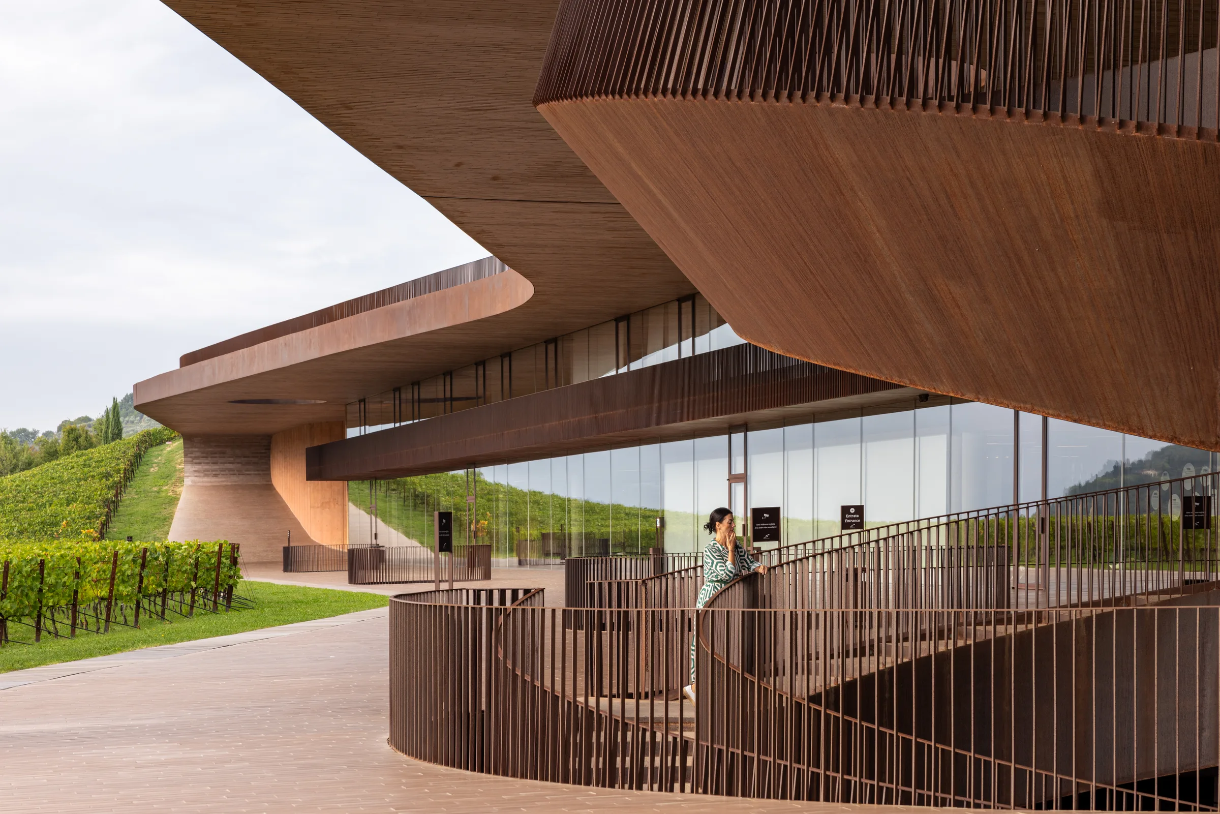 Woman leaning on a railing of Cantina Antinori's spiral staircase, with the cantilevered roof and vineyard behind her, Tuscany, by ARCHTRAITS