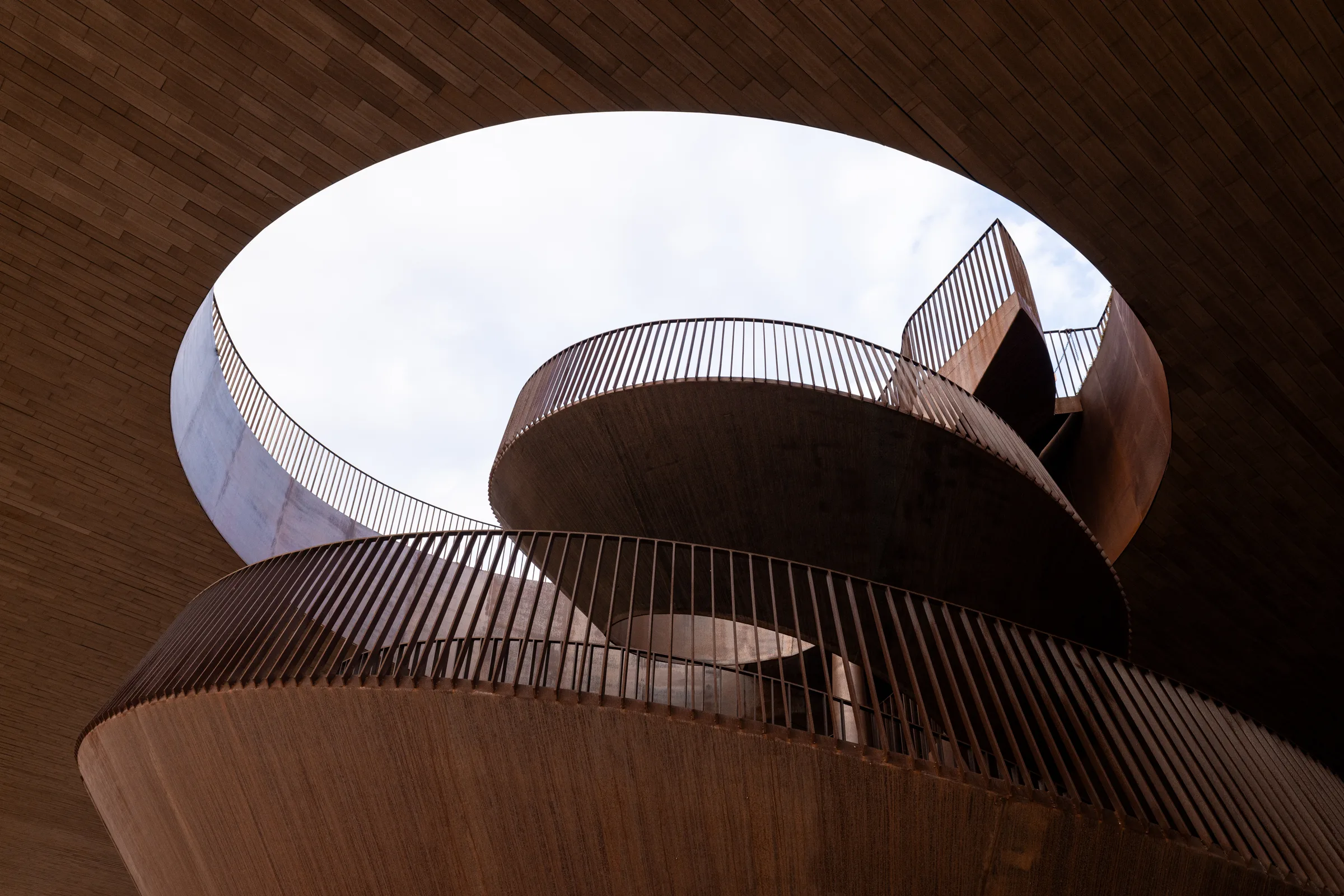 Looking up at Cantina Antinori's spiraling corten steel staircase and oval skylight, Tuscany, by ARCHTRAITS