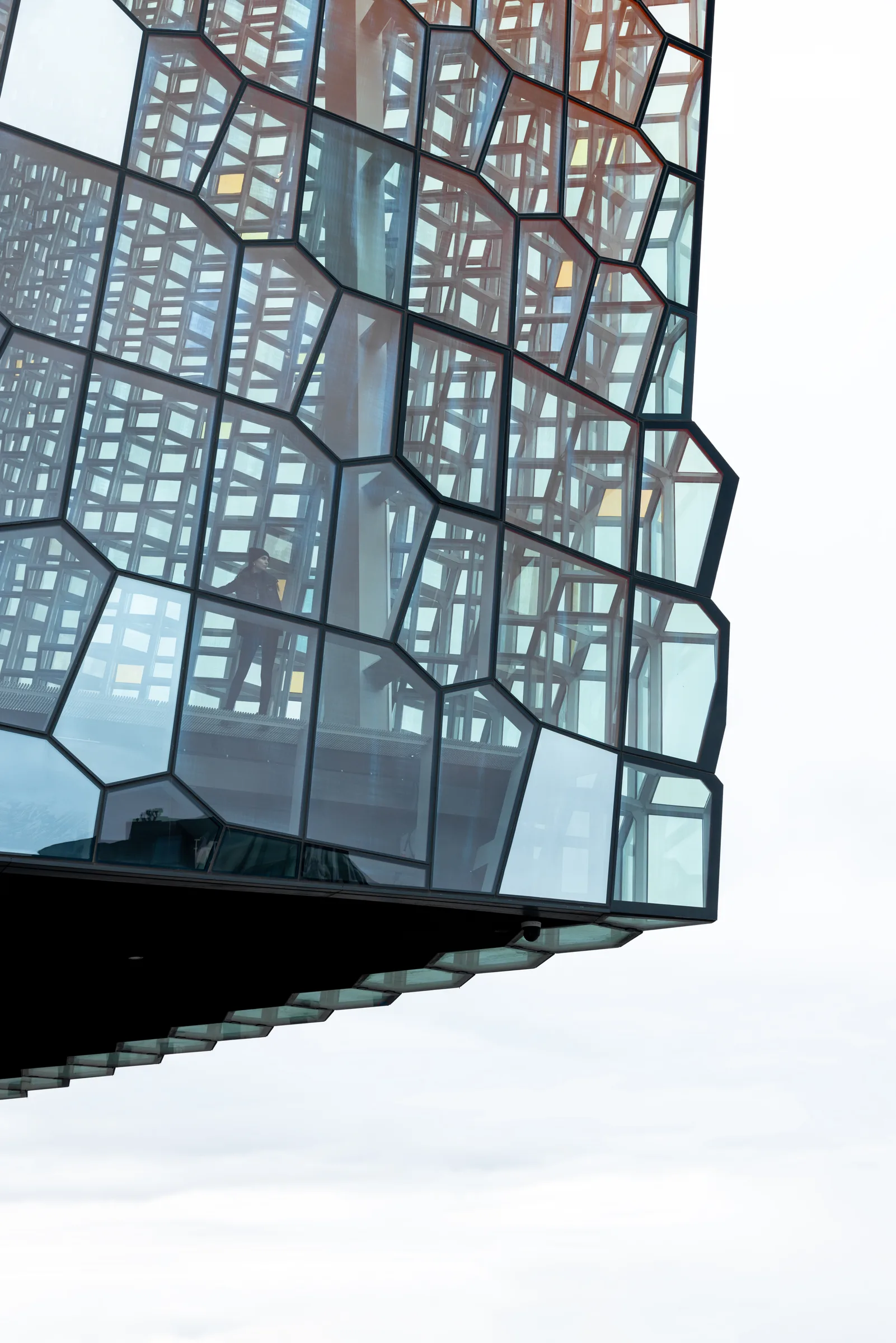 Close-up of Harpa Concert Hall's honeycomb glass facade with a figure silhouetted inside, Reykjavik, by ARCHTRAITS