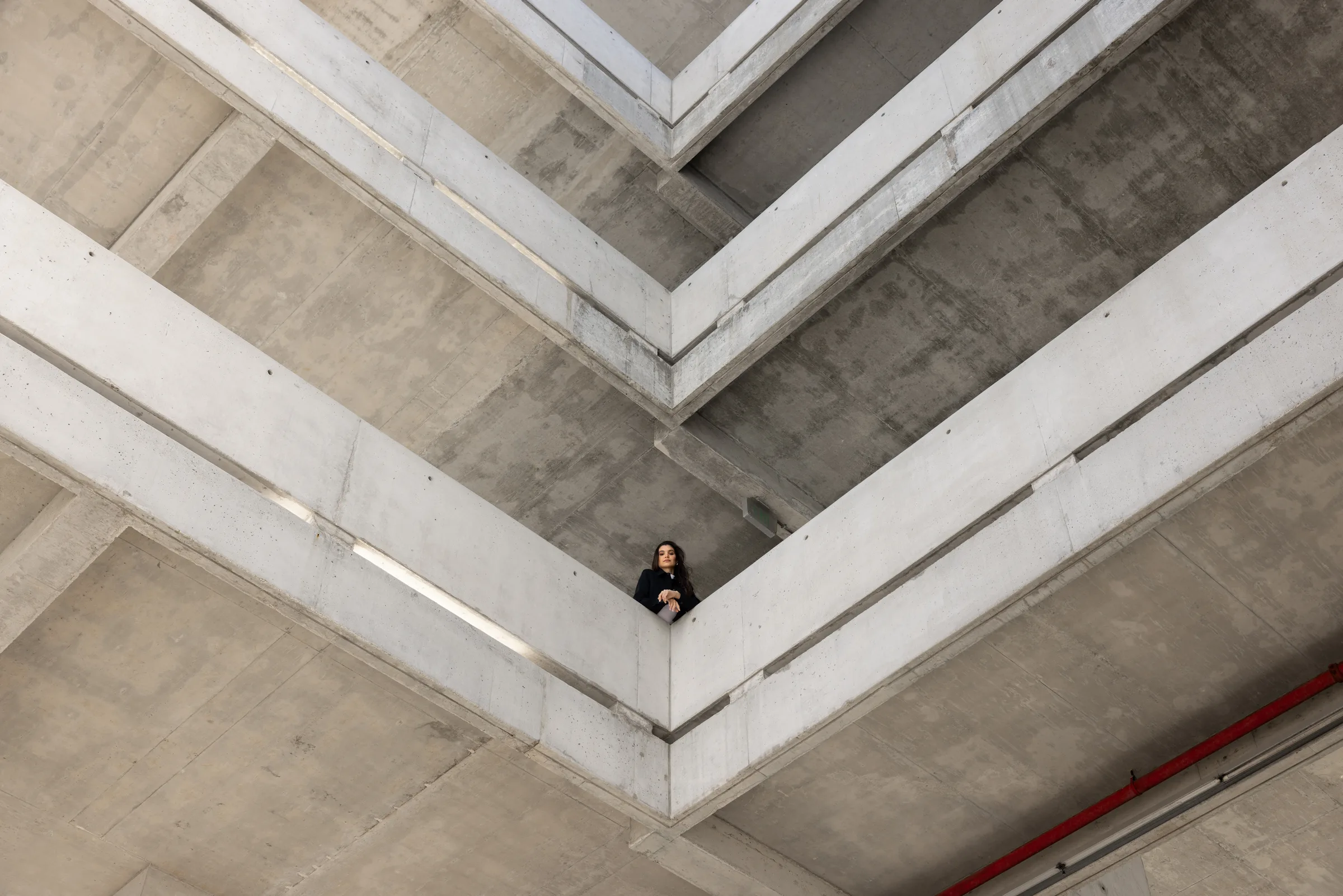 Woman standing on a balcony framed by converging concrete beams at Miami Dade College, Florida, by ARCHTRAITS