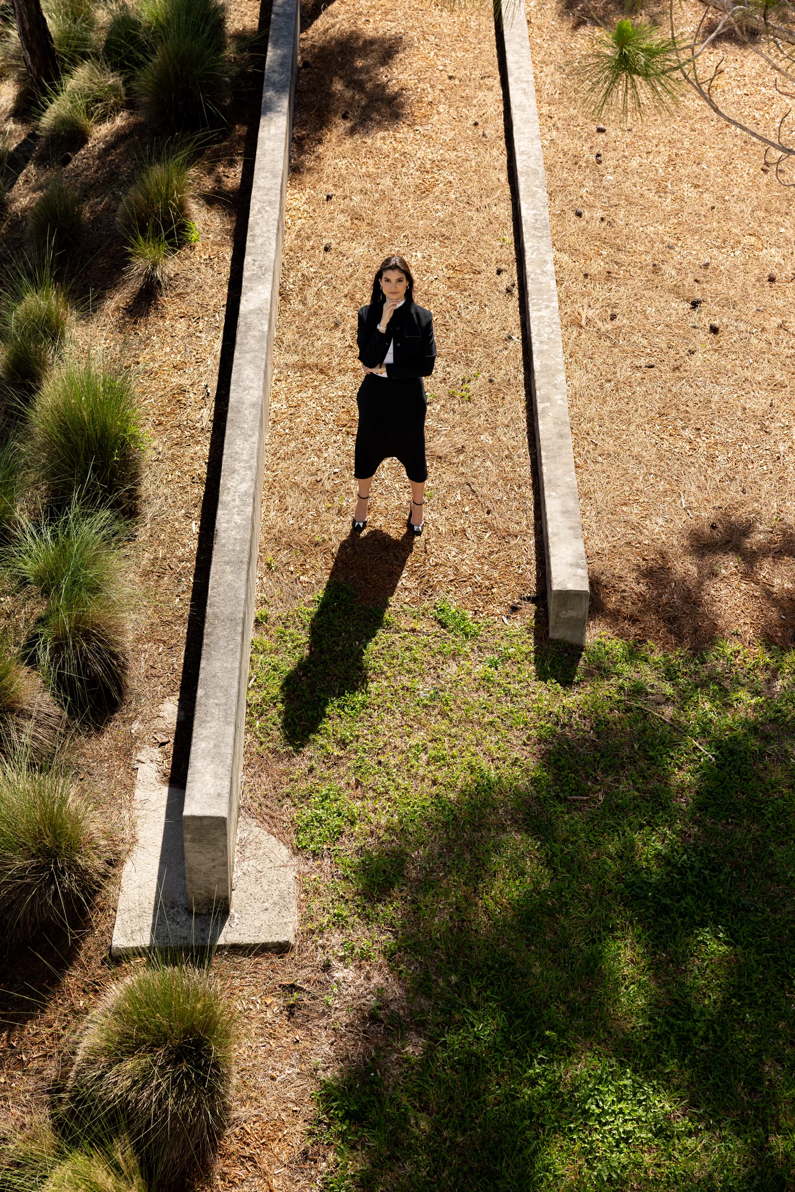 Aerial view of a woman walking across a paved plaza beneath a lamppost shadow at Miami Dade College, Florida, by ARCHTRAITS