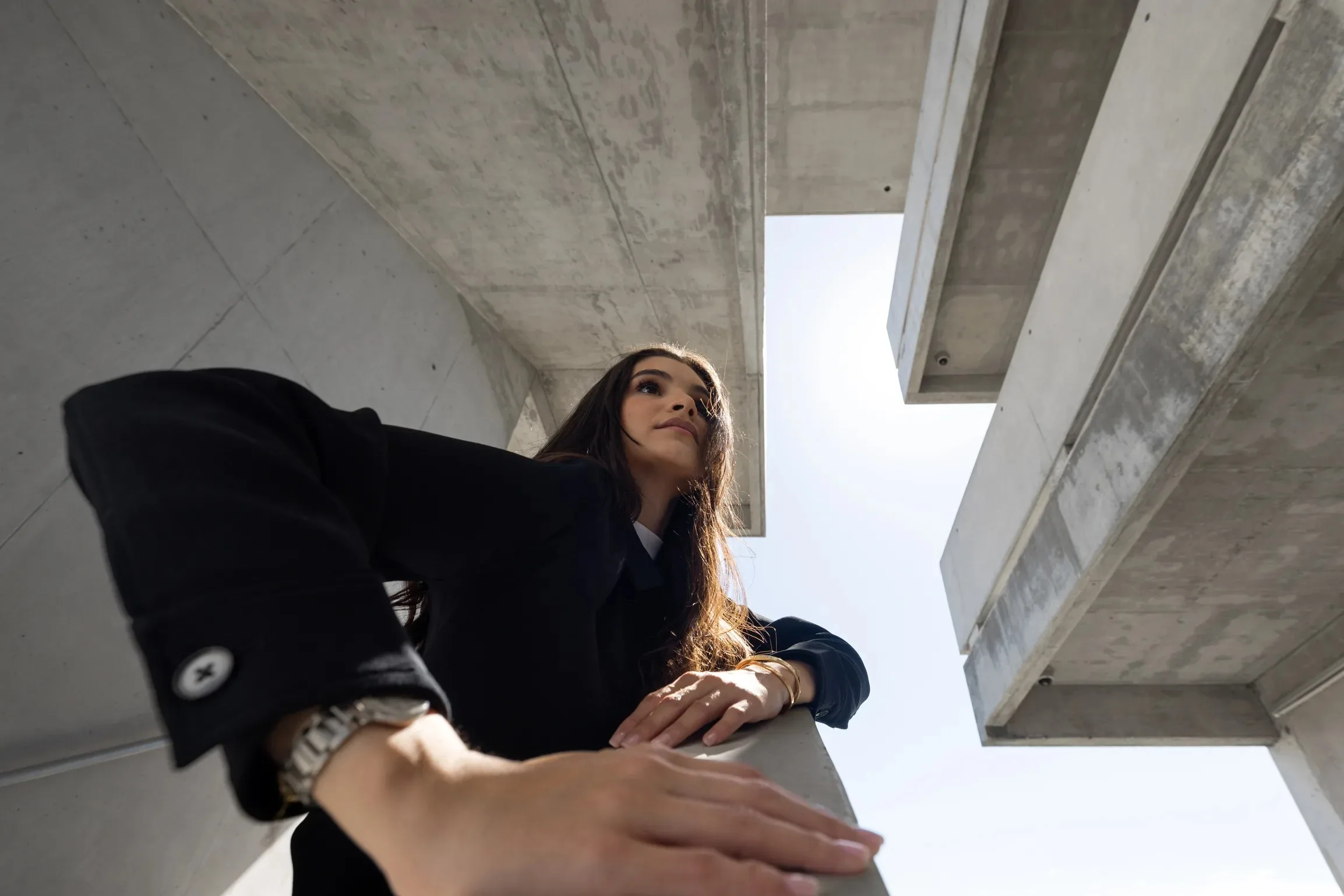 Low-angle view looking up at a woman leaning over a concrete railing amid converging cantilevered beams, Miami Dade College, Florida, by ARCHTRAITS
