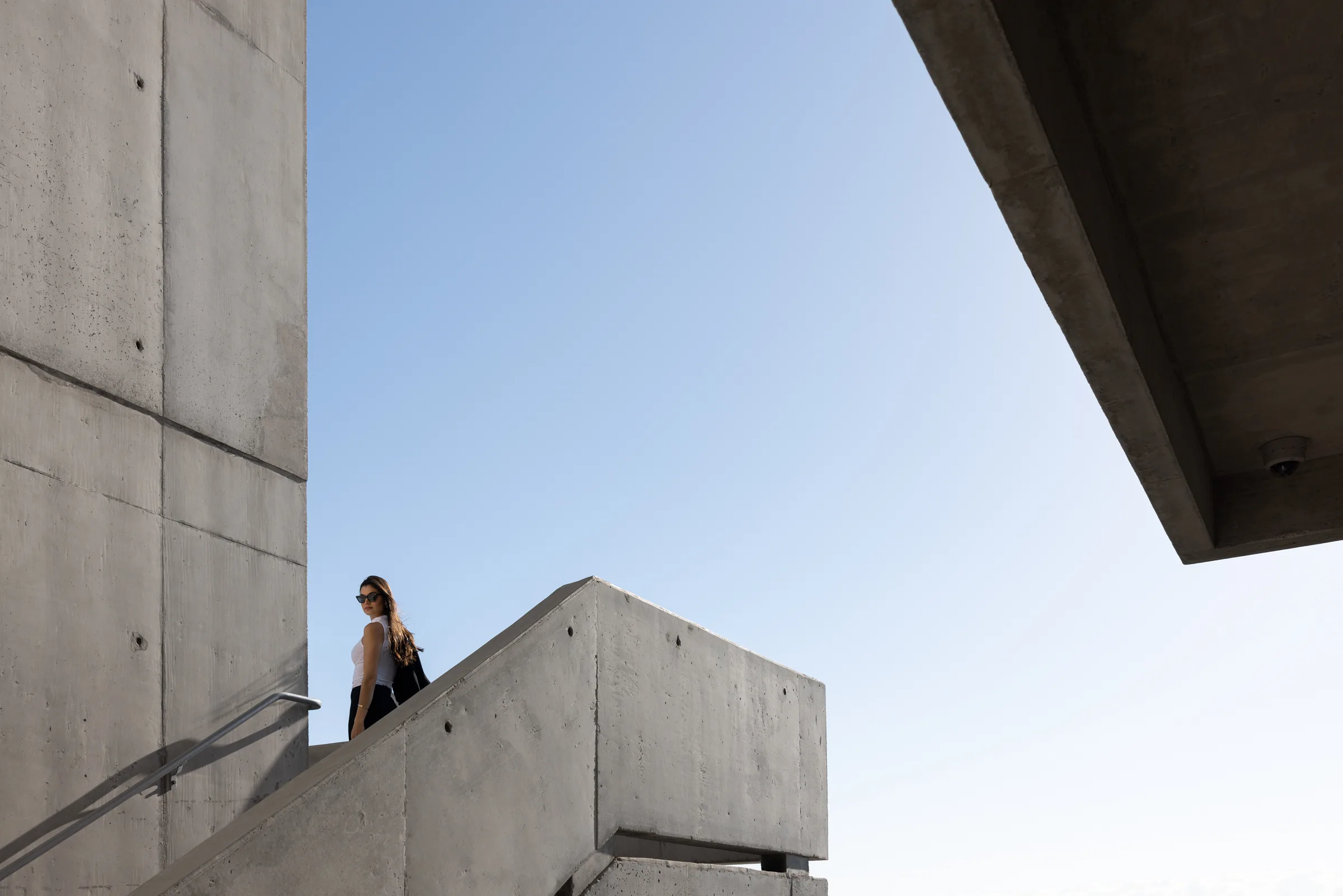 Woman standing at a staircase landing amid the concrete structure of Miami Dade College, Florida, by ARCHTRAITS
