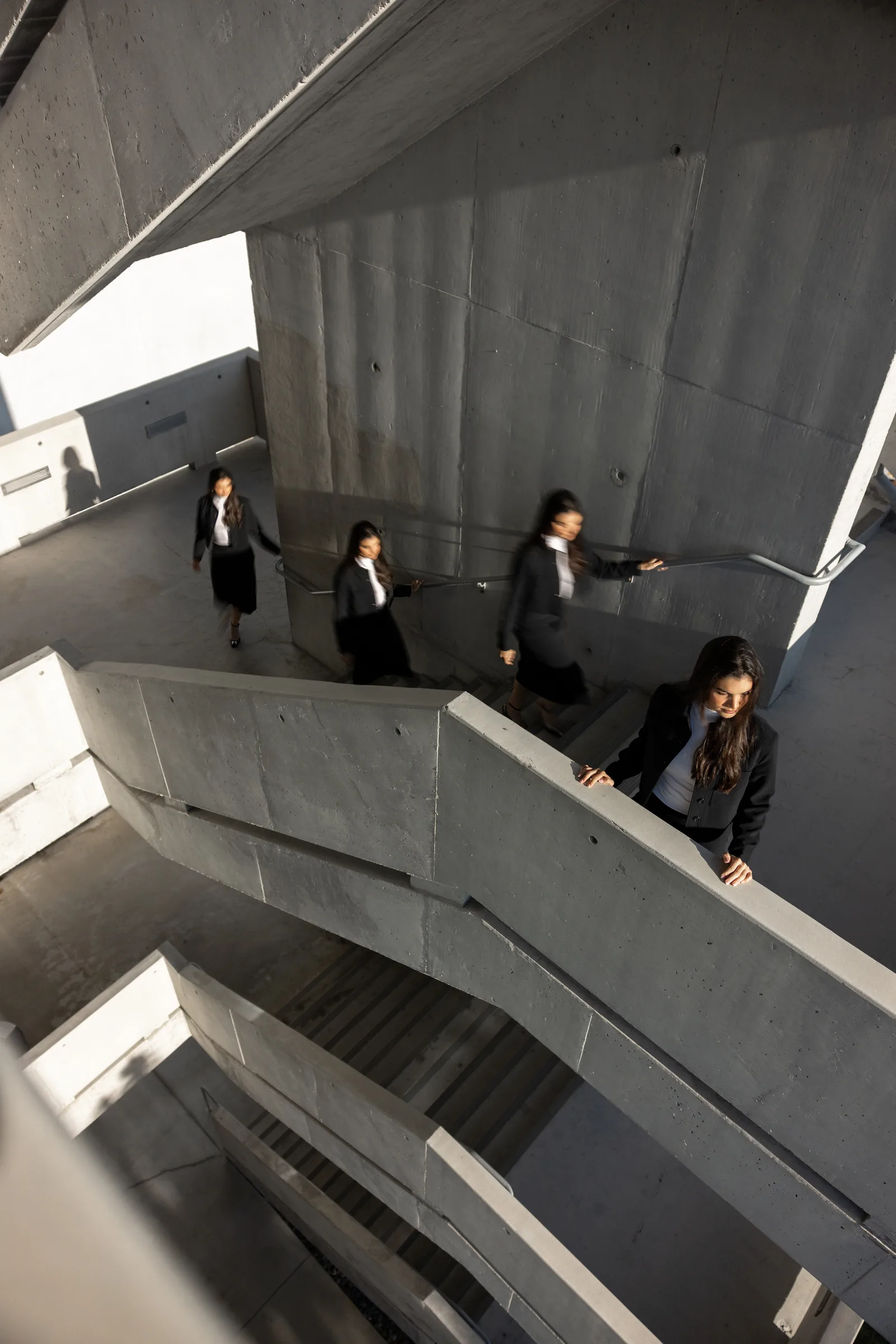 Woman in sunglasses standing atop an angular concrete staircase against a clear sky at Miami Dade College, Florida, by ARCHTRAITS