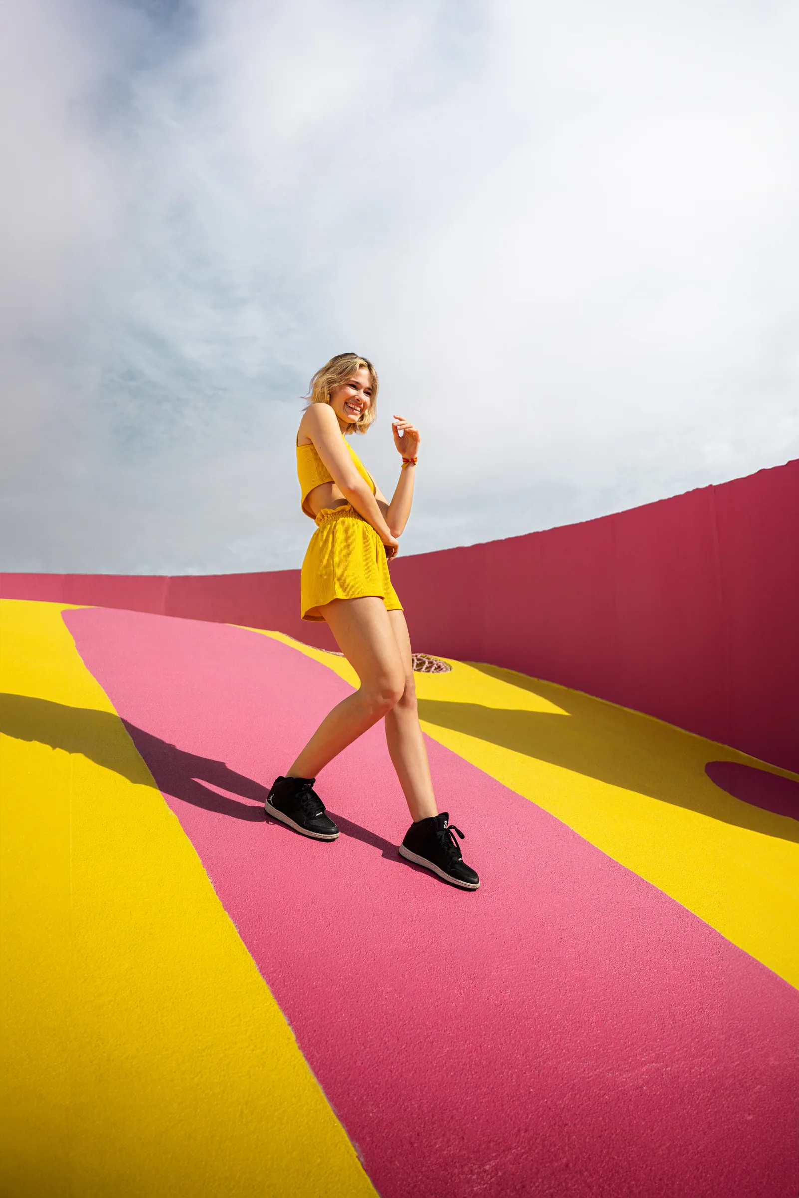 Woman in yellow standing on Museum Garage's pink-and-yellow striped rooftop, Miami Design District, by ARCHTRAITS