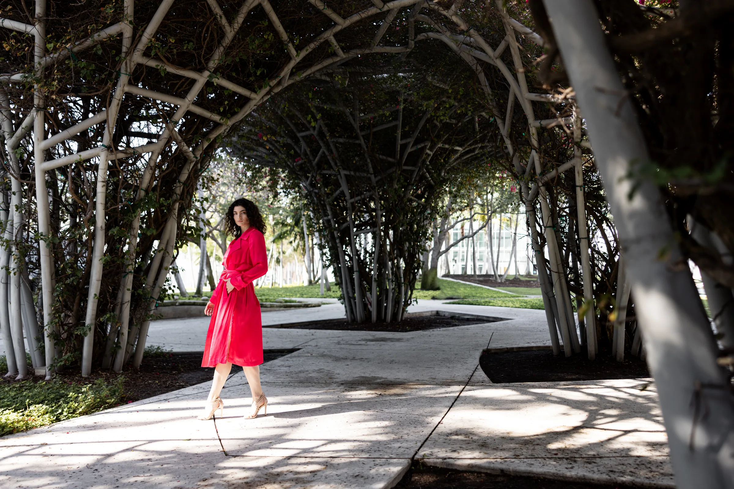 Woman in a red coat walking through the bougainvillea-covered trellis tunnel at New World Center's SoundScape Park, Miami Beach, by ARCHTRAITS